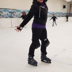 A woman is ice skating on a rink with her arms outstretched.