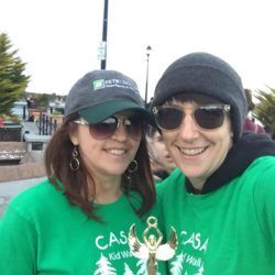 Two women wearing green shirts and hats are posing for a picture.