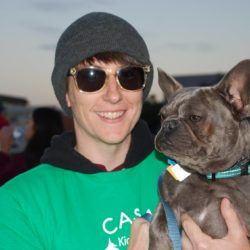 A man wearing a green casa shirt is holding a dog