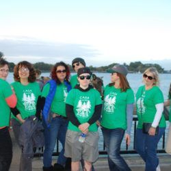 A group of people wearing green shirts are standing in front of a body of water.