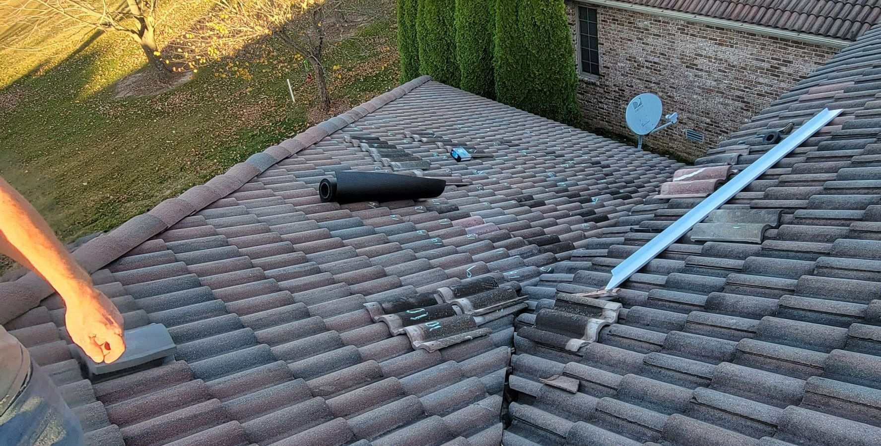 Person on a tiled roof near chimney and antenna; daytime.