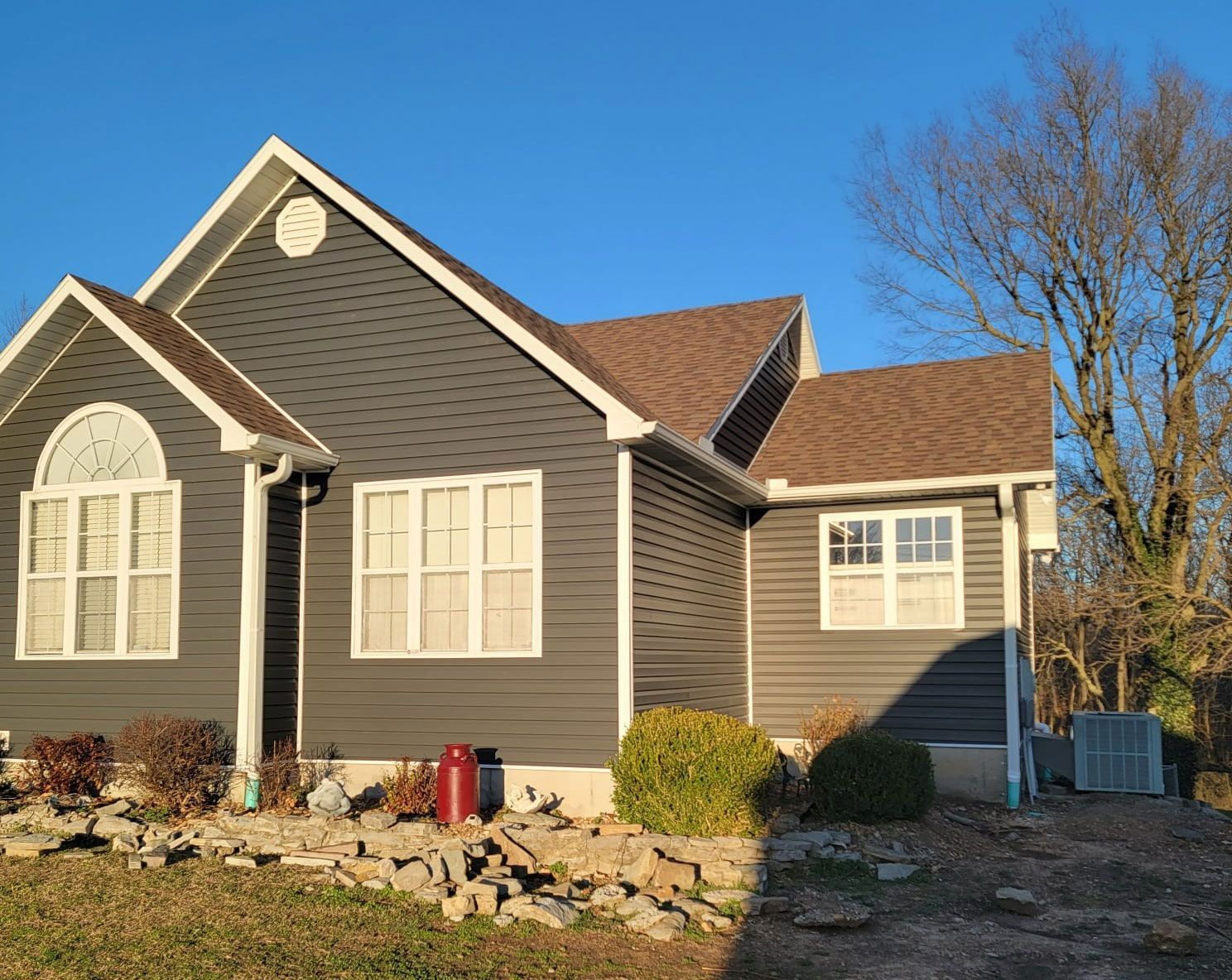 Dark gray house with white trim, brown roof, clear blue sky, and a small yard.