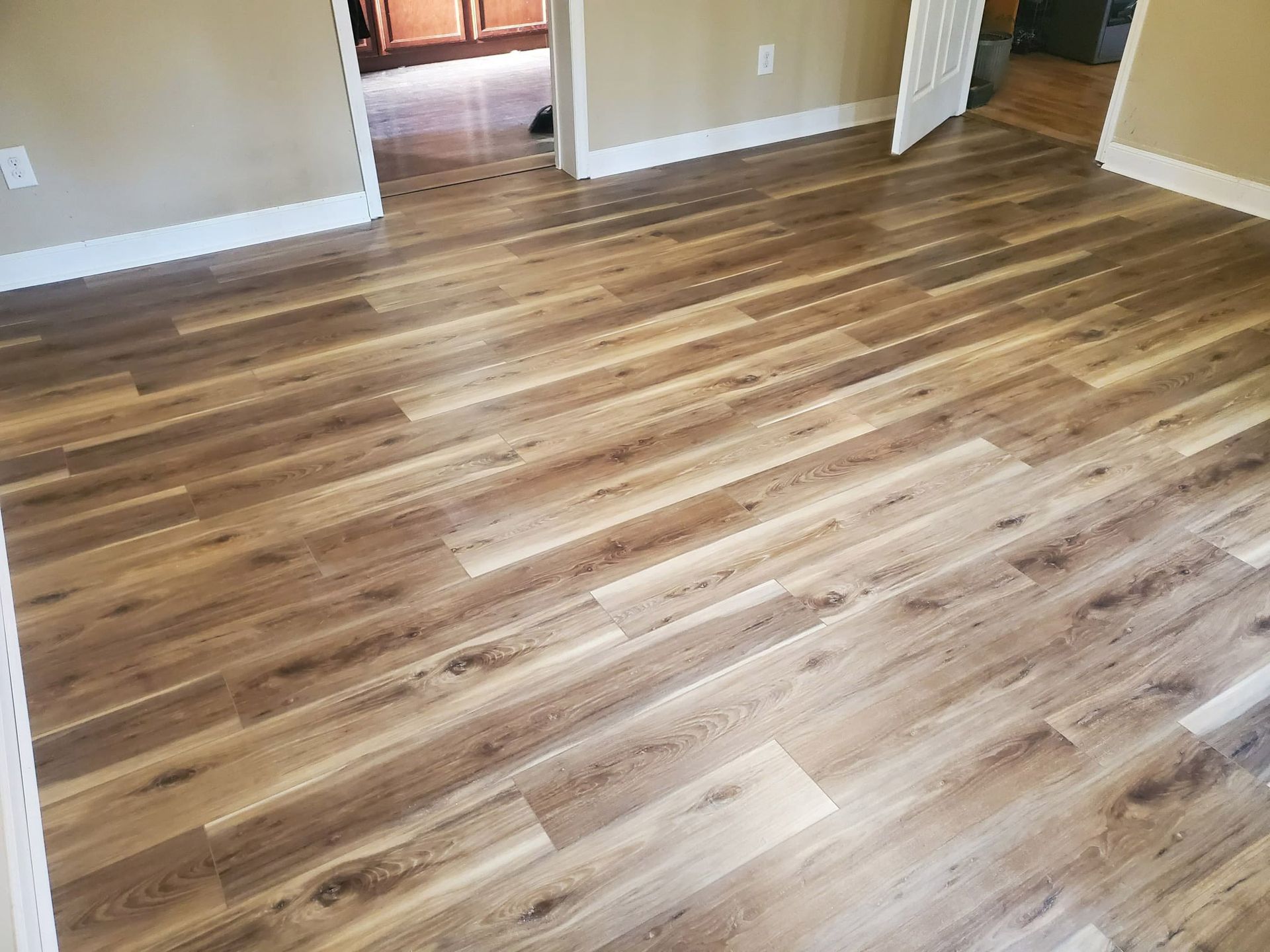 Hardwood-like flooring in a room with light brown and beige tones; white baseboards and tan walls.