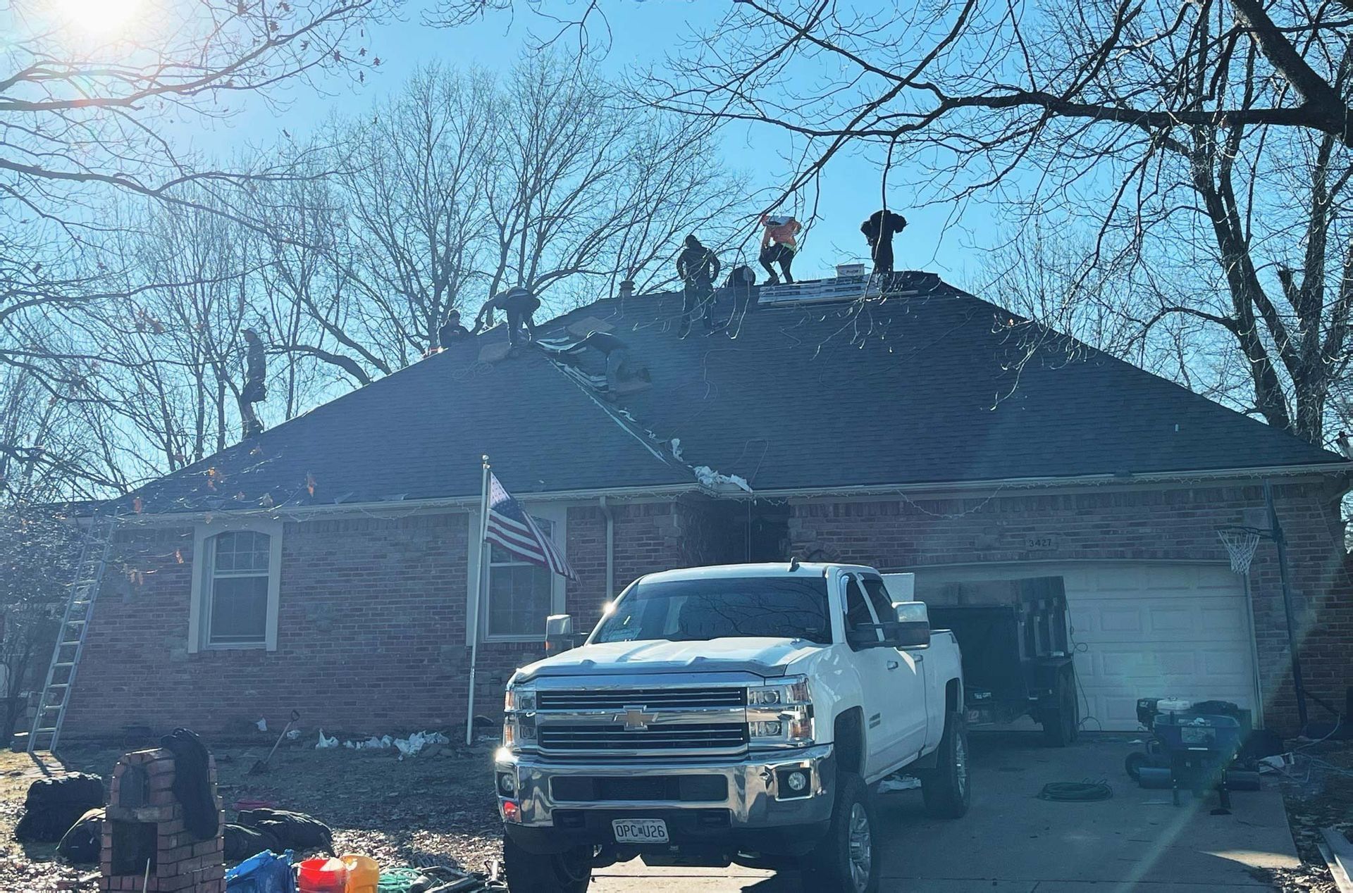 Roofers on a house roof with a truck parked in front.
