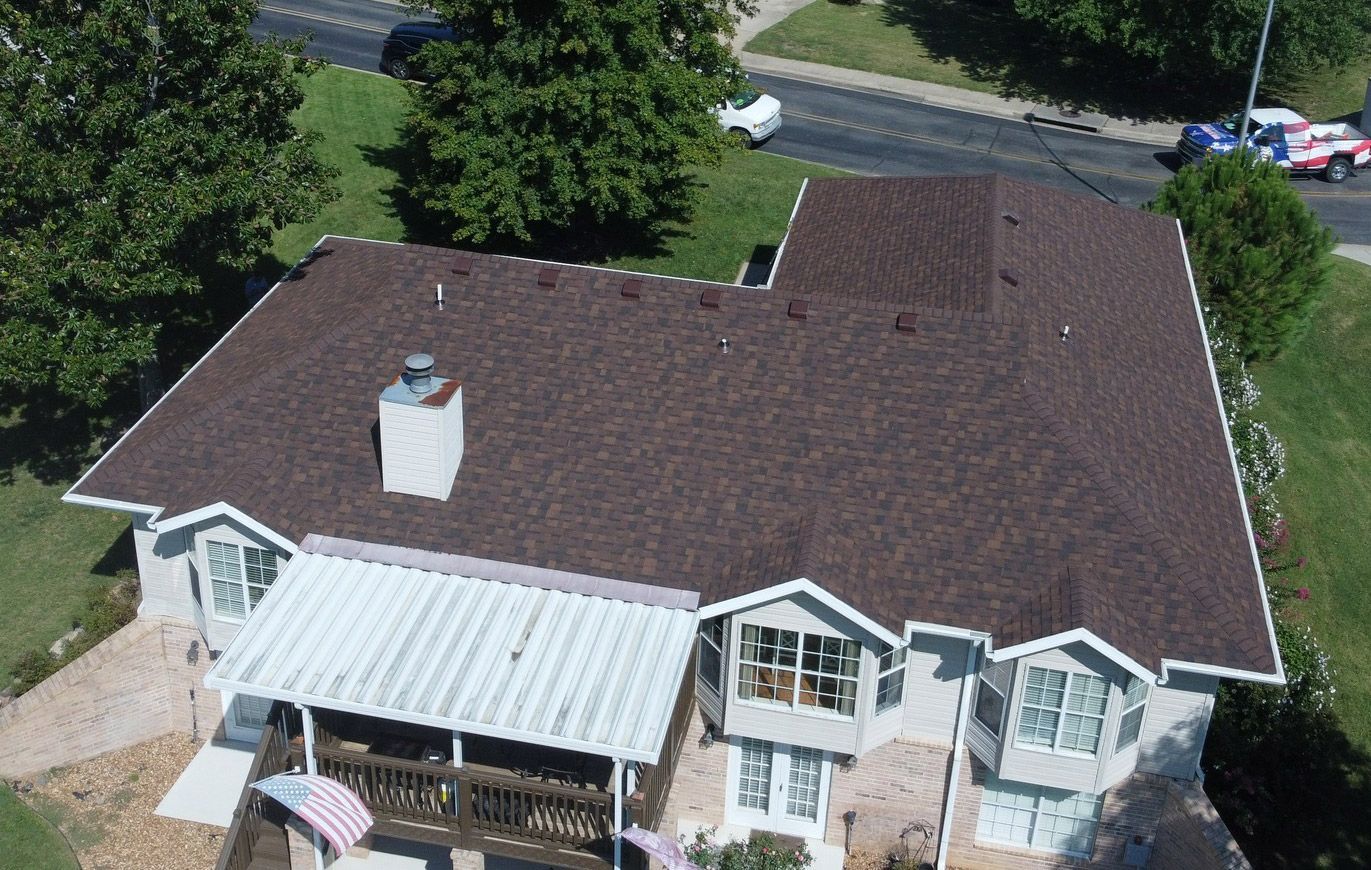 Aerial view of a house with a brown shingled roof, a white chimney, and a white porch roof.