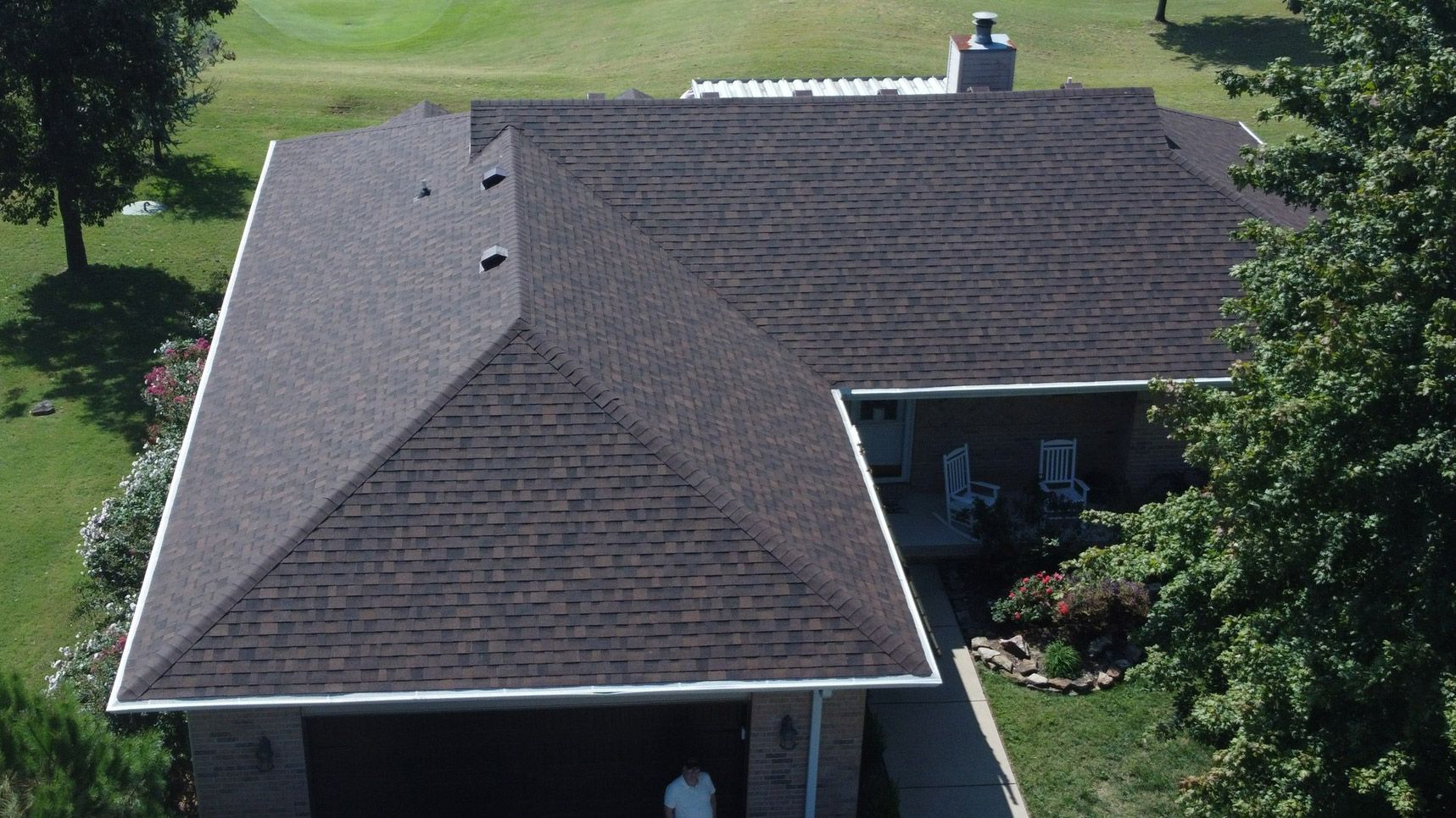 Brown shingle roof on a house with a green lawn and trees.