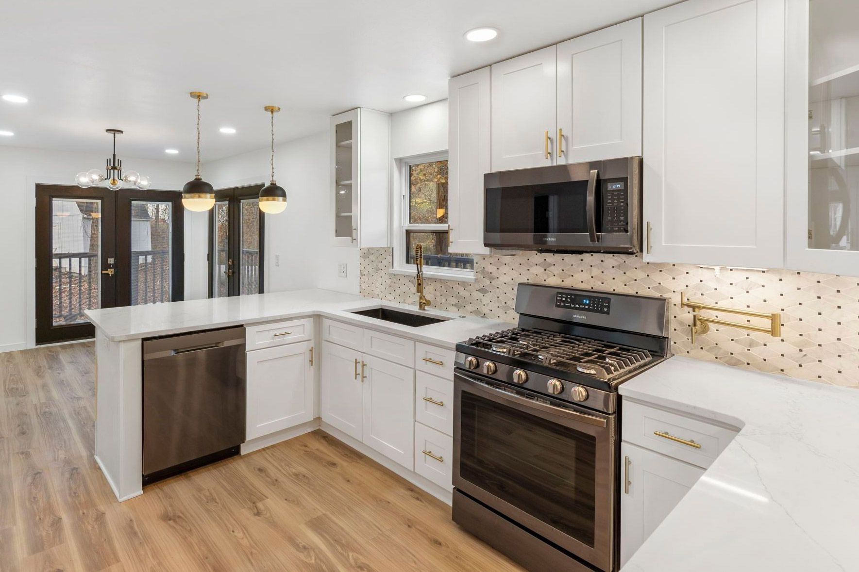 Modern white kitchen with stainless steel appliances, light wood floors, and gold accents.