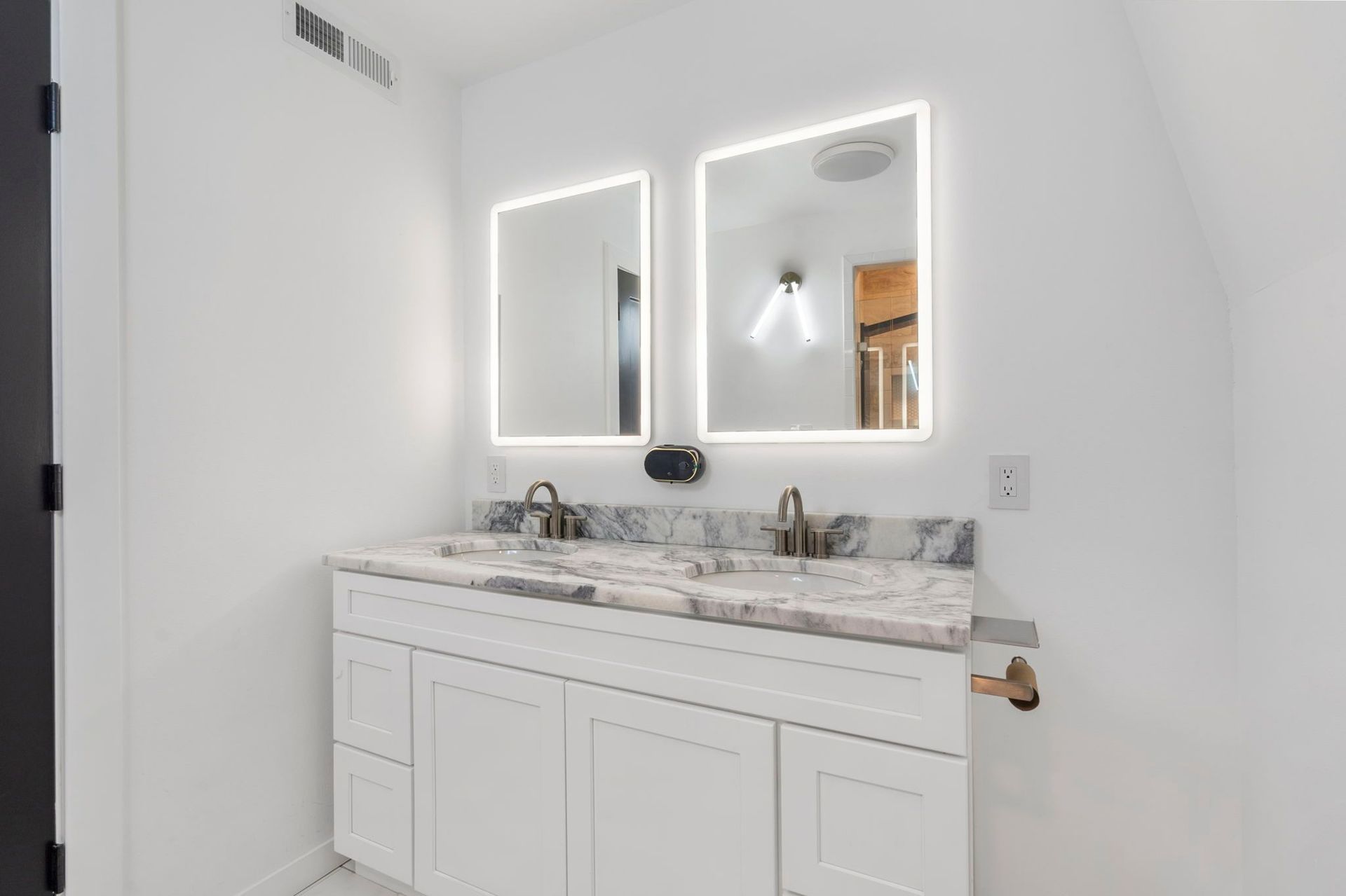 White bathroom with double vanity, marble countertop, two illuminated mirrors.