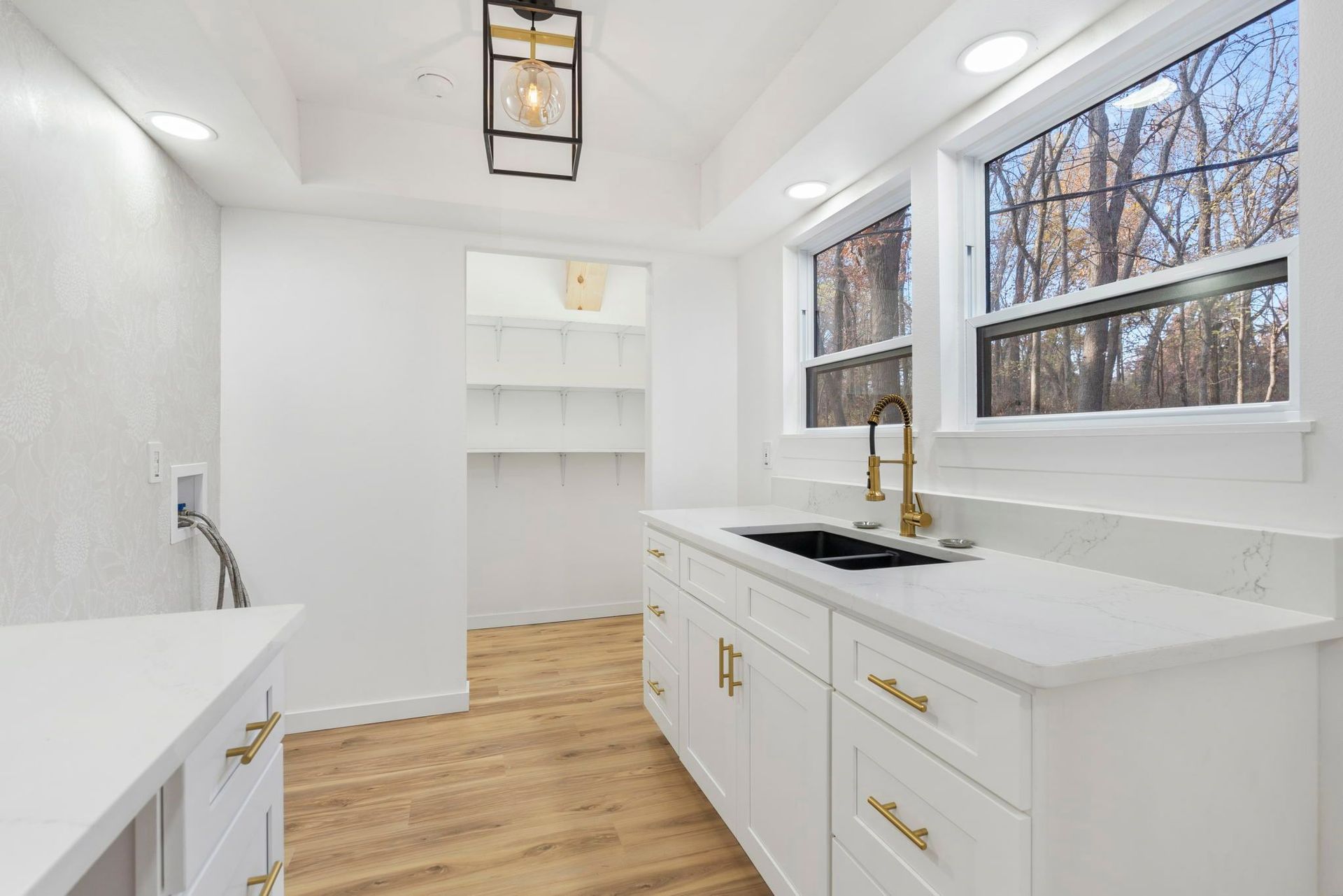White kitchen with marble countertops, gold hardware, and a window overlooking trees.