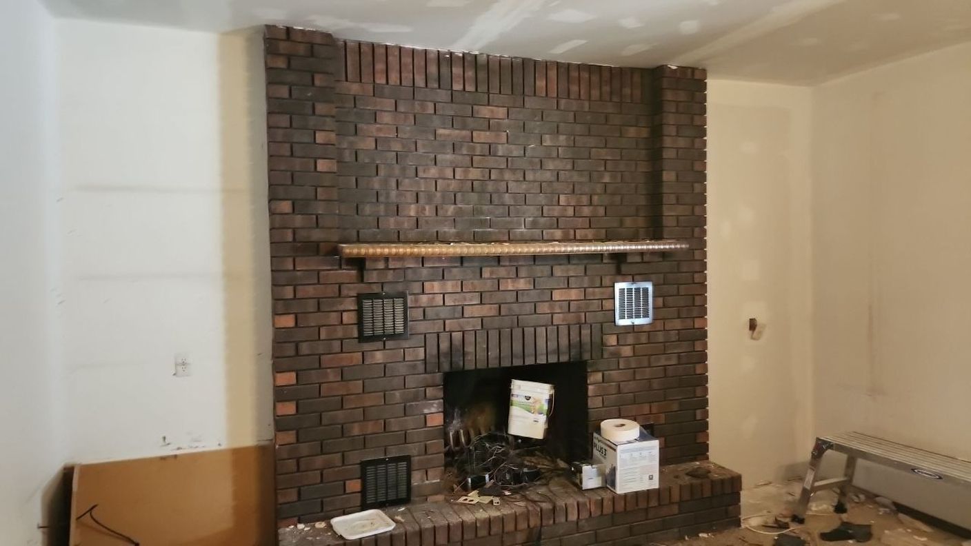 Brick fireplace in a room, with a wooden mantel, papers, and debris in the hearth.