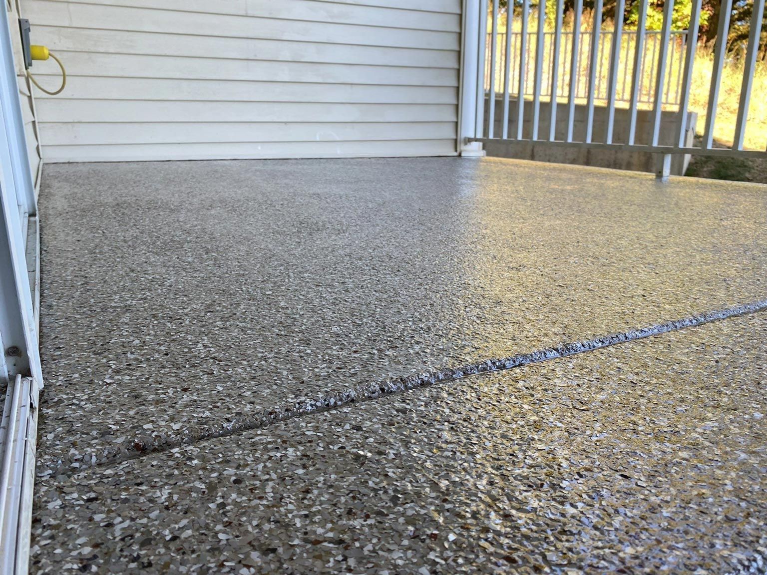 Gray speckled patio with white siding and railing.