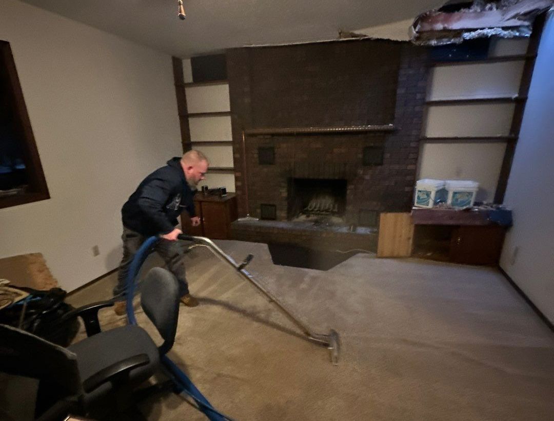 Man cleaning carpet in a room with a brick fireplace and built-in shelves.
