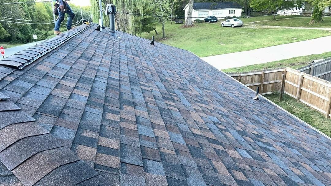 Roofers working on a newly shingled roof with a brown and black pattern.