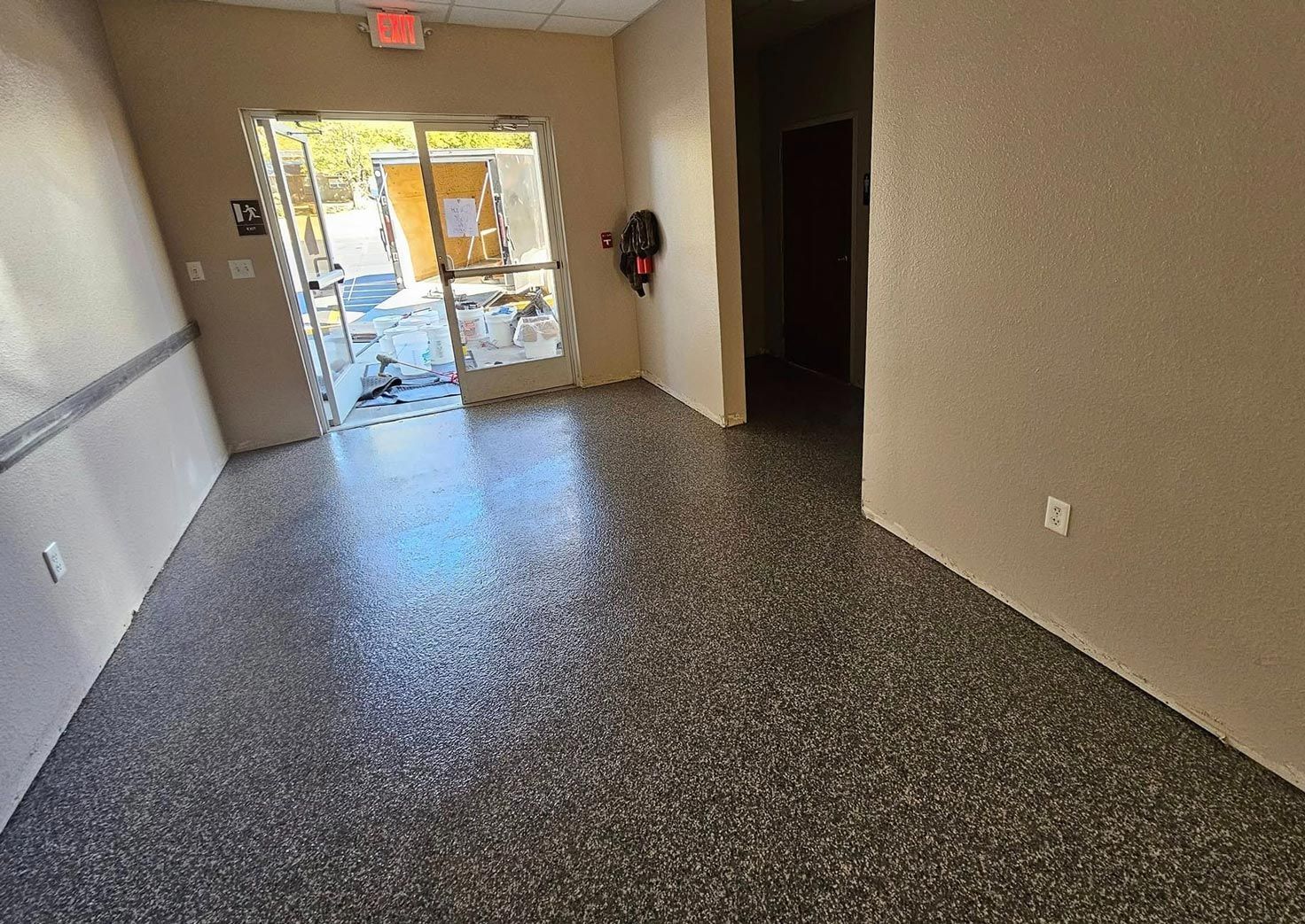 Interior view with speckled flooring leading to a doorway and hallway; neutral colors.
