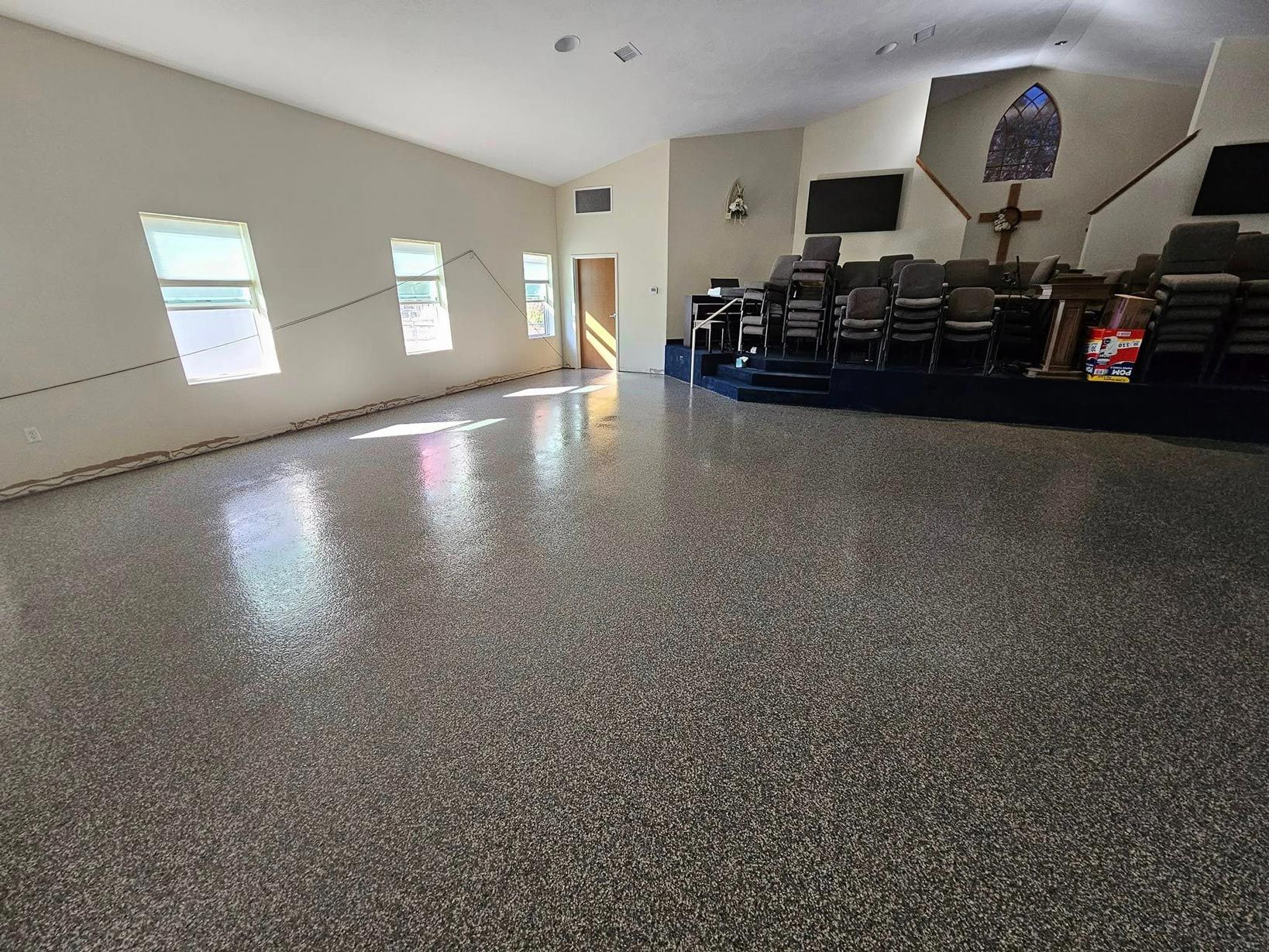 Church interior with a glossy, speckled floor; pews; cross, and stained glass.
