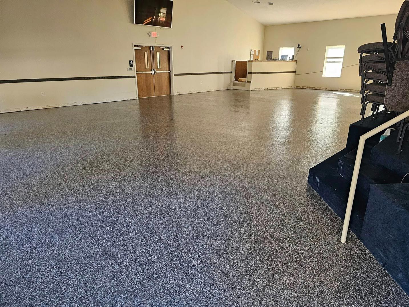 Indoor view of a room with a speckled epoxy floor. Walls are white and doors are wood-colored.