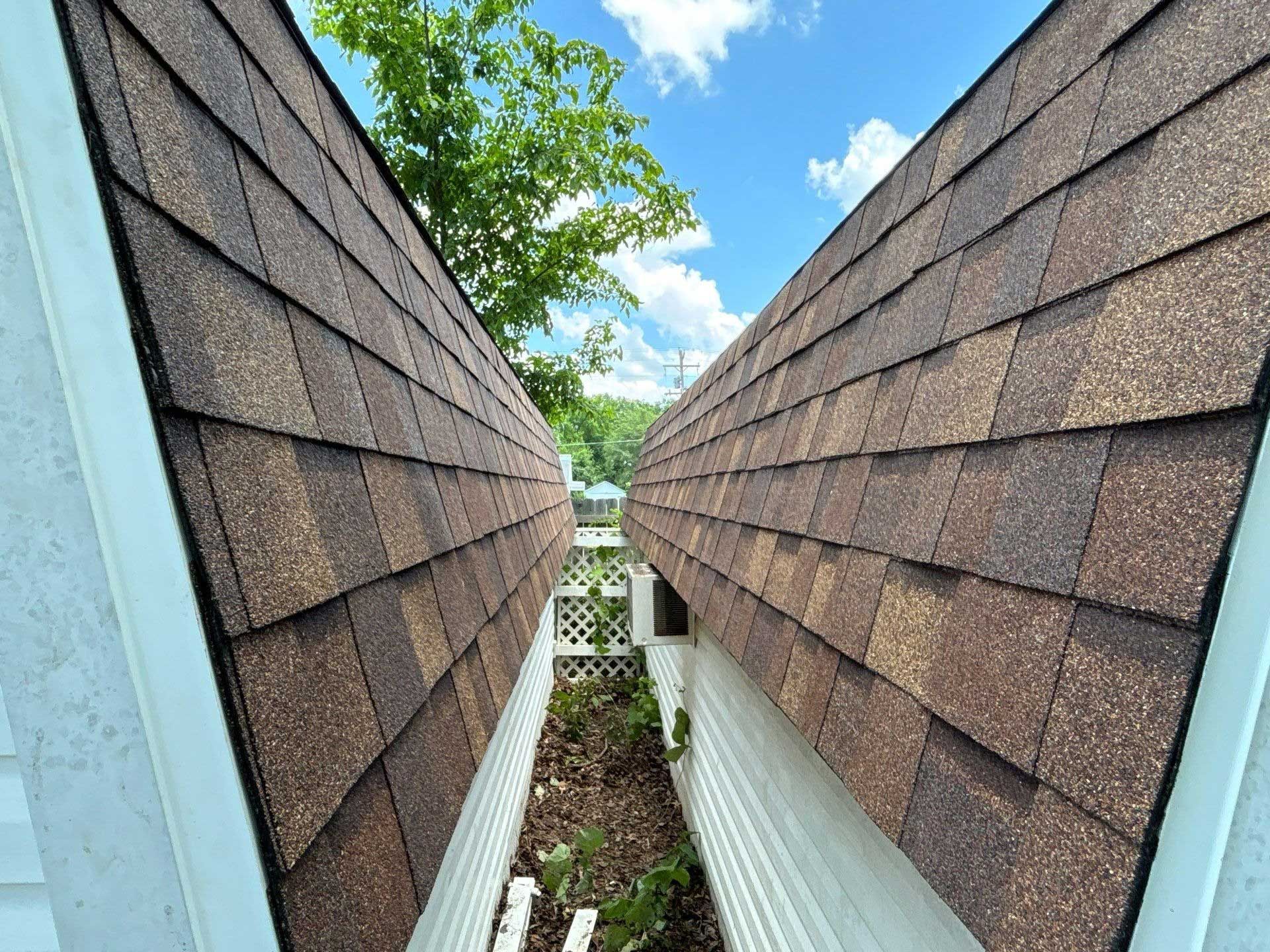 Two brown shingled rooftops facing each other, with a narrow space in between, blue sky visible.