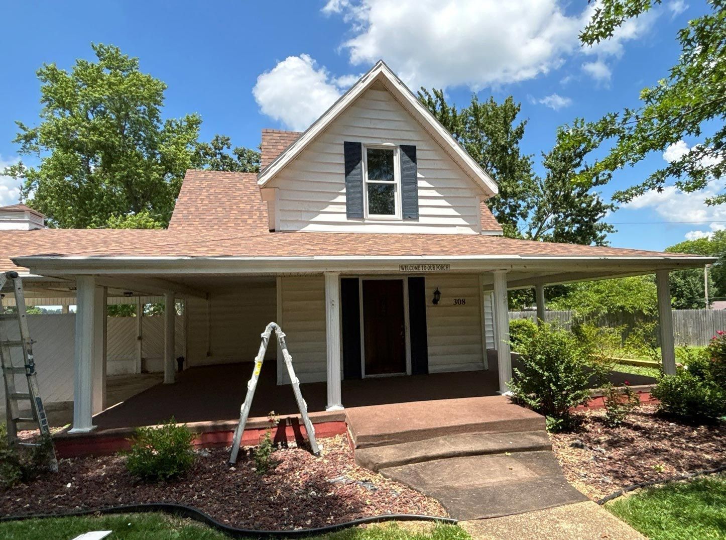 Tan two-story house with a porch and new brown roof. Blue sky with trees.