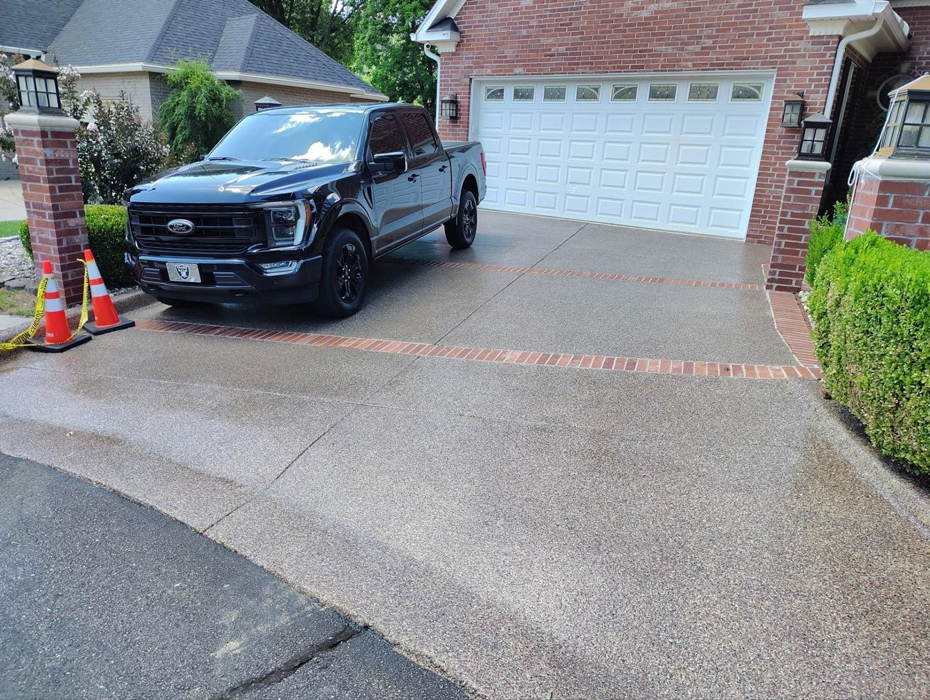 Black truck parked on a wet, speckled driveway in front of a brick house with a white garage door.