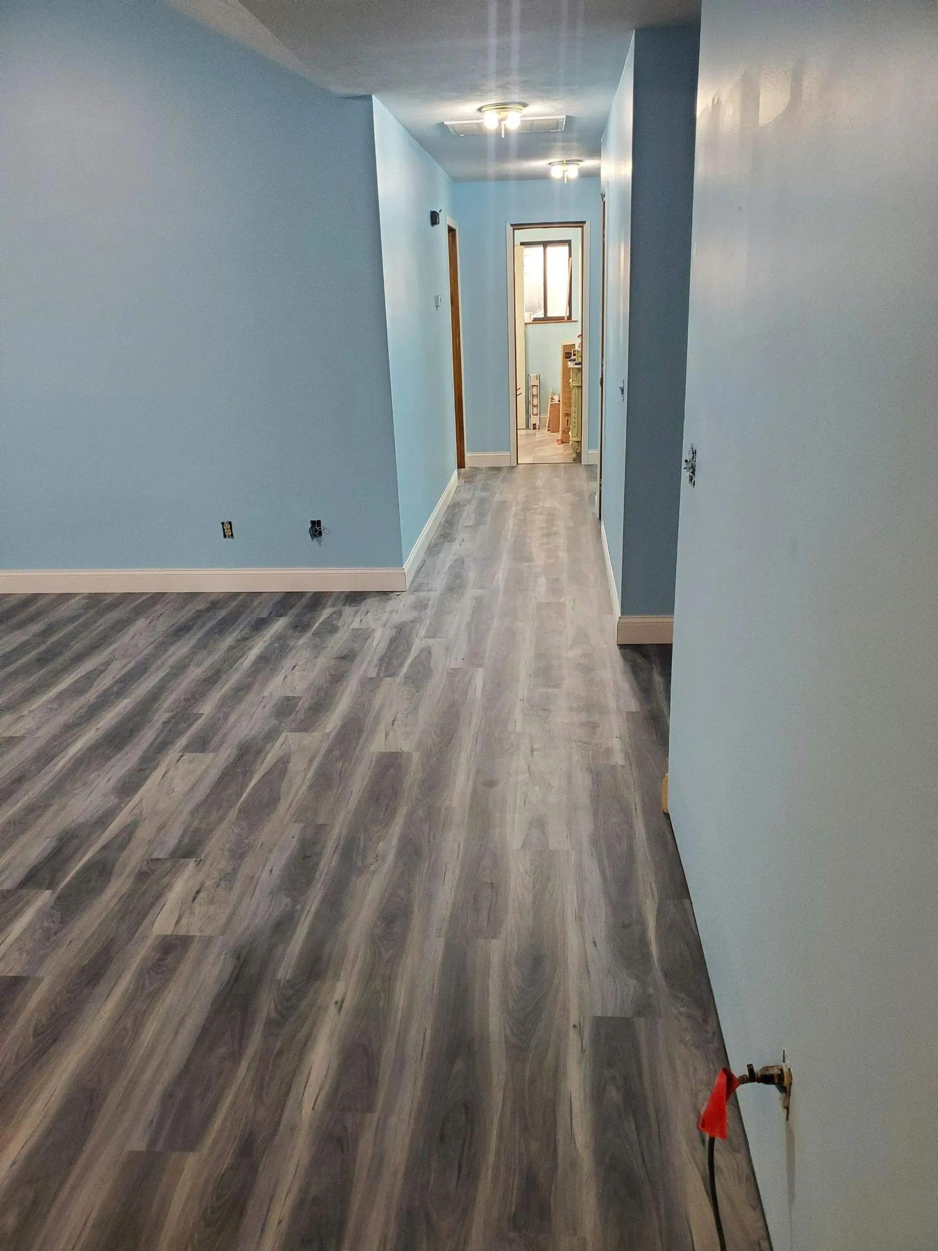 Long hallway with light blue walls, gray wood-look flooring, and a door at the end.