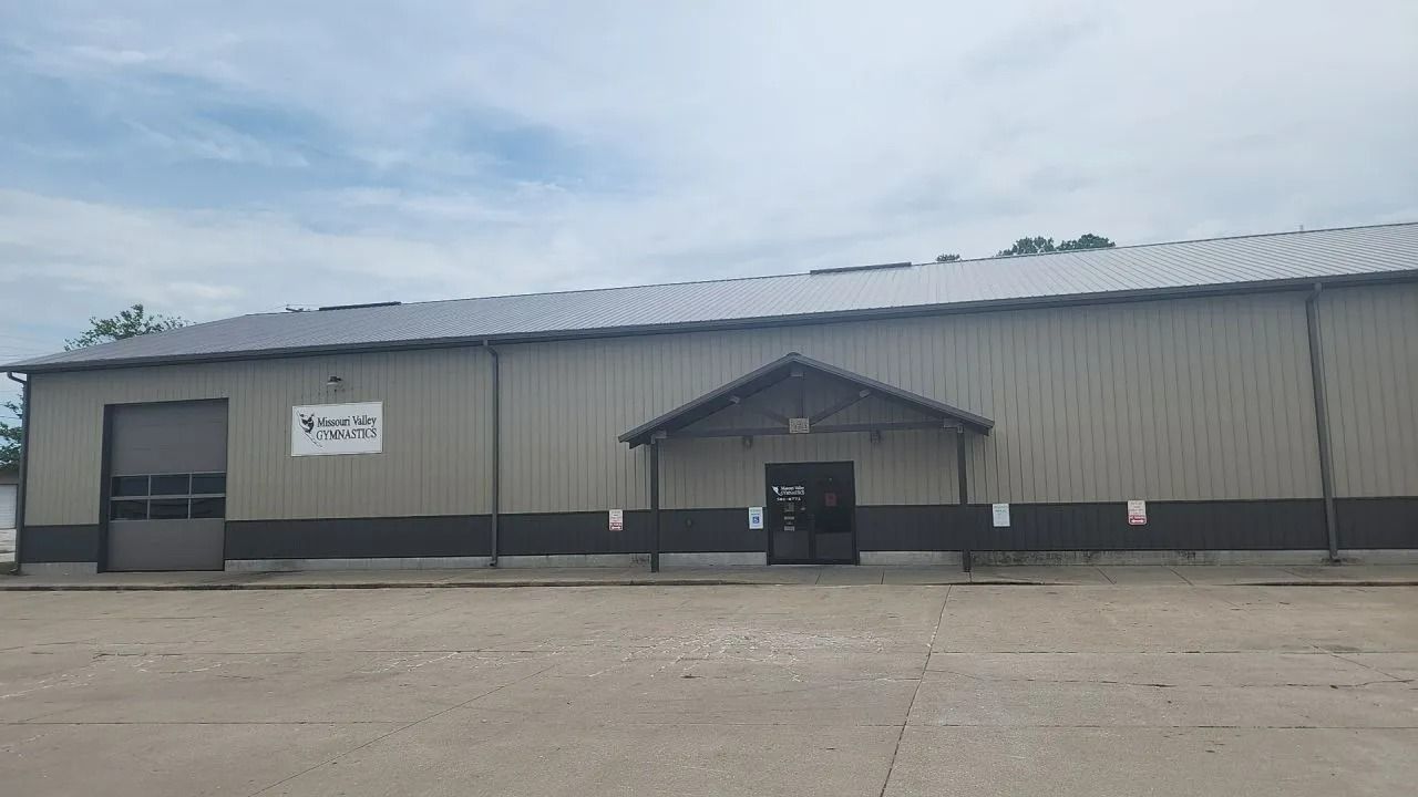 Gray industrial building with a garage door and covered entrance under a cloudy sky.
