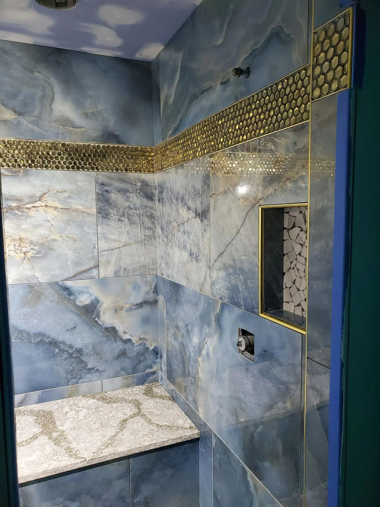 Blue tiled shower with gold accents, mosaic trim, and a built-in shelf.