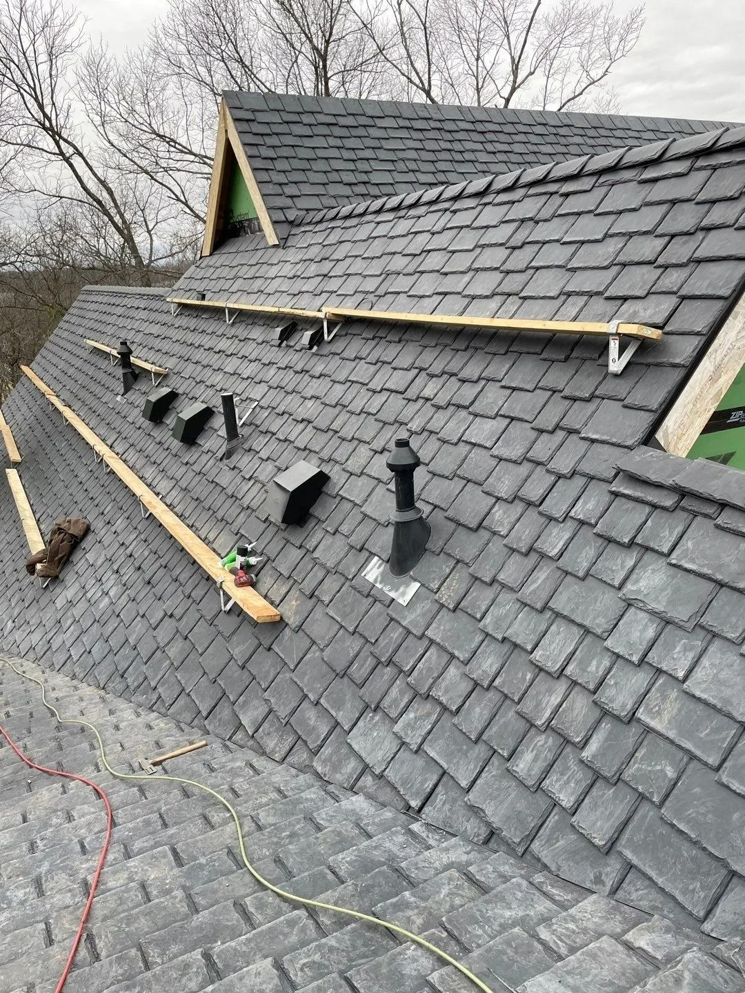 Dark gray shingle roof under construction with roof vents and wood supports.