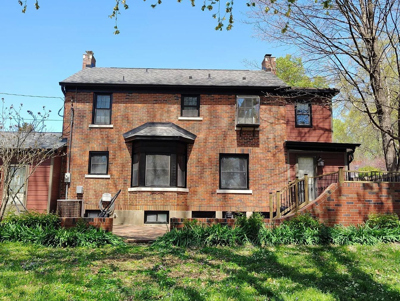 Brick house with several windows, including a bay window, set in a yard with grass and trees.
