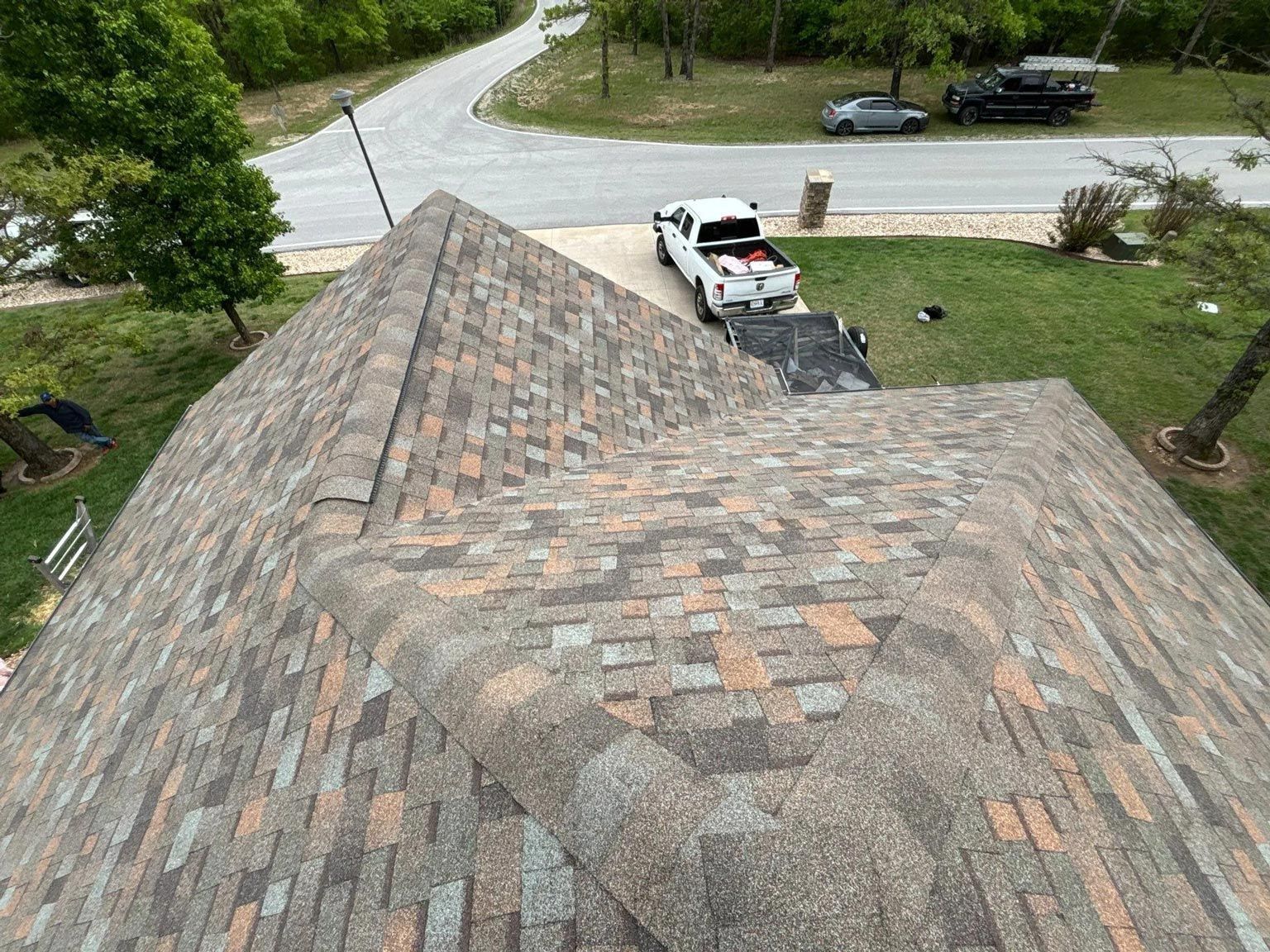 Overhead view of a house roof with multicolored shingles, a driveway, and a pickup truck parked.
