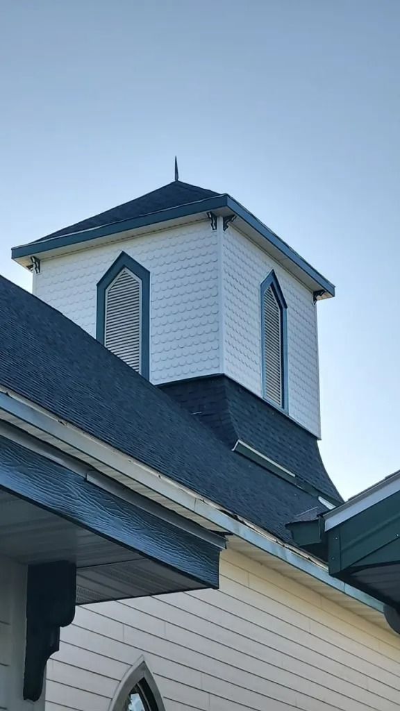 White church steeple with arched windows, blue roof against a clear sky.