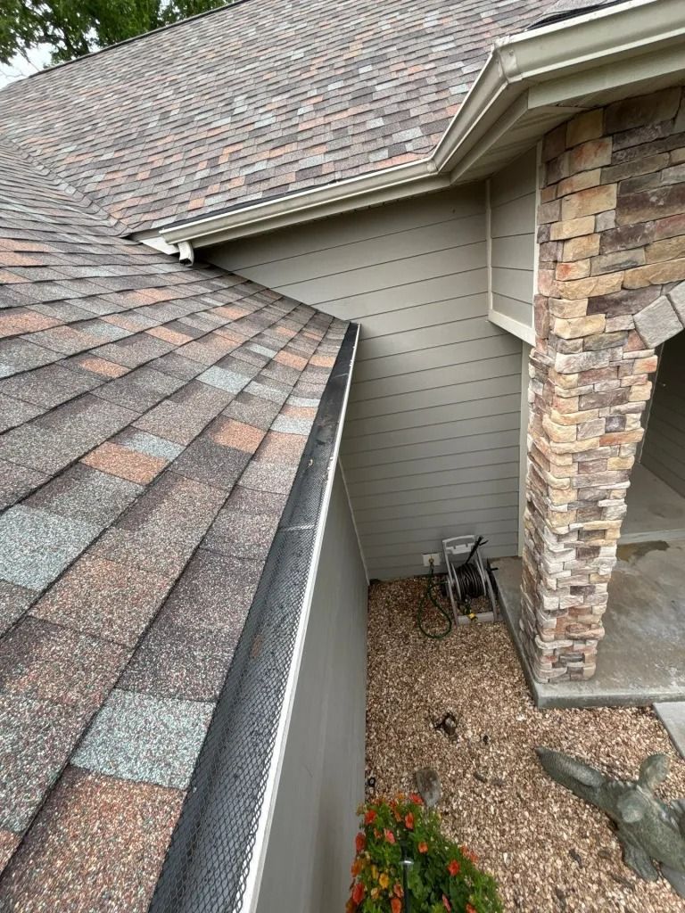 Overhead view of a roof with a gutter and siding next to a stone pillar, set outdoors.
