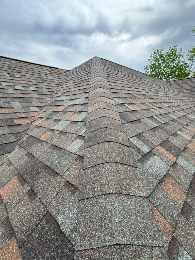 Close-up of a multi-colored asphalt shingle roof against a cloudy sky.