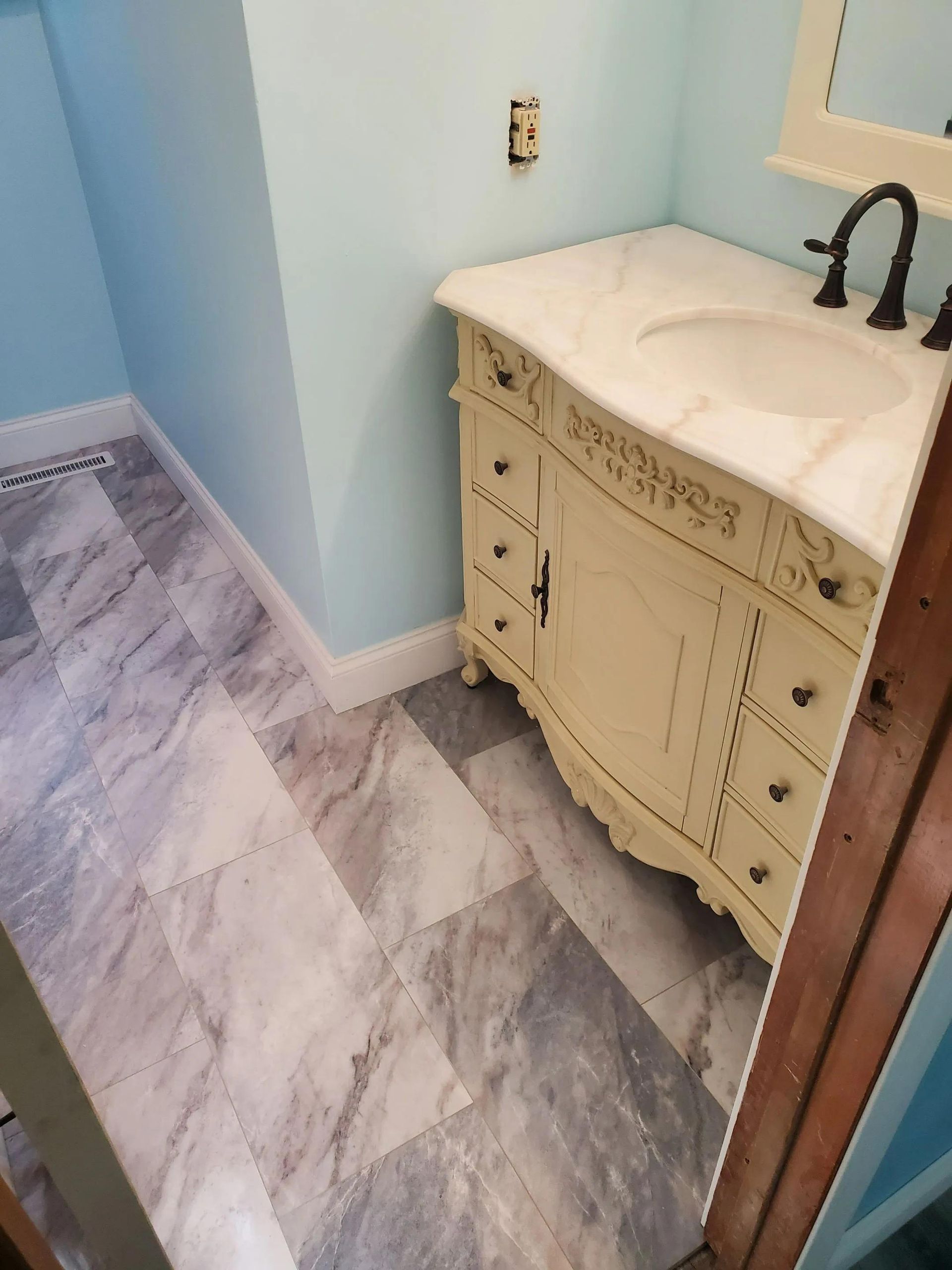 Bathroom with light blue walls, marble-look floor, and off-white vanity with a white countertop.