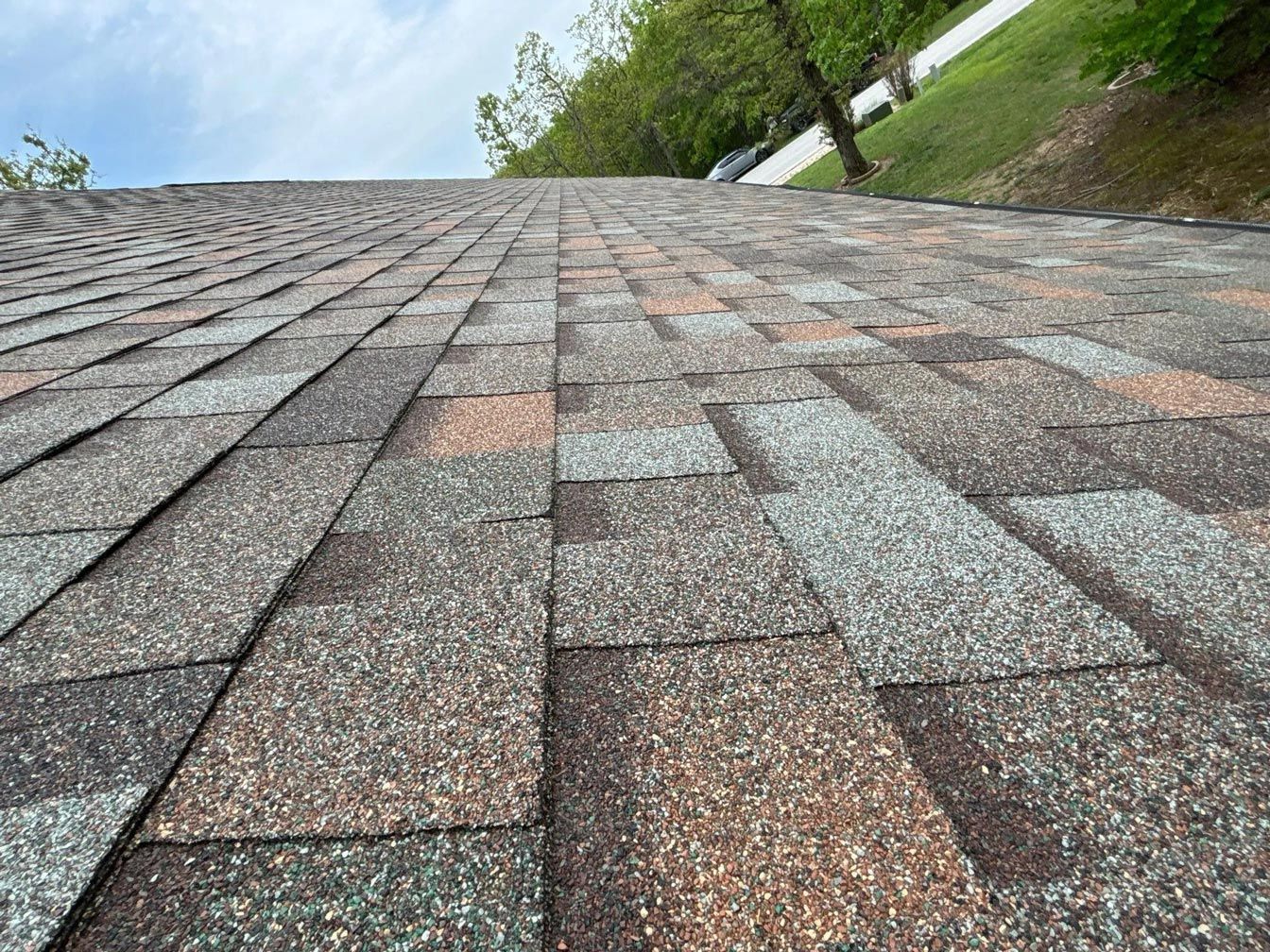 Close-up view of a shingle roof with various shades of brown, gray, and orange, angled towards the sky.