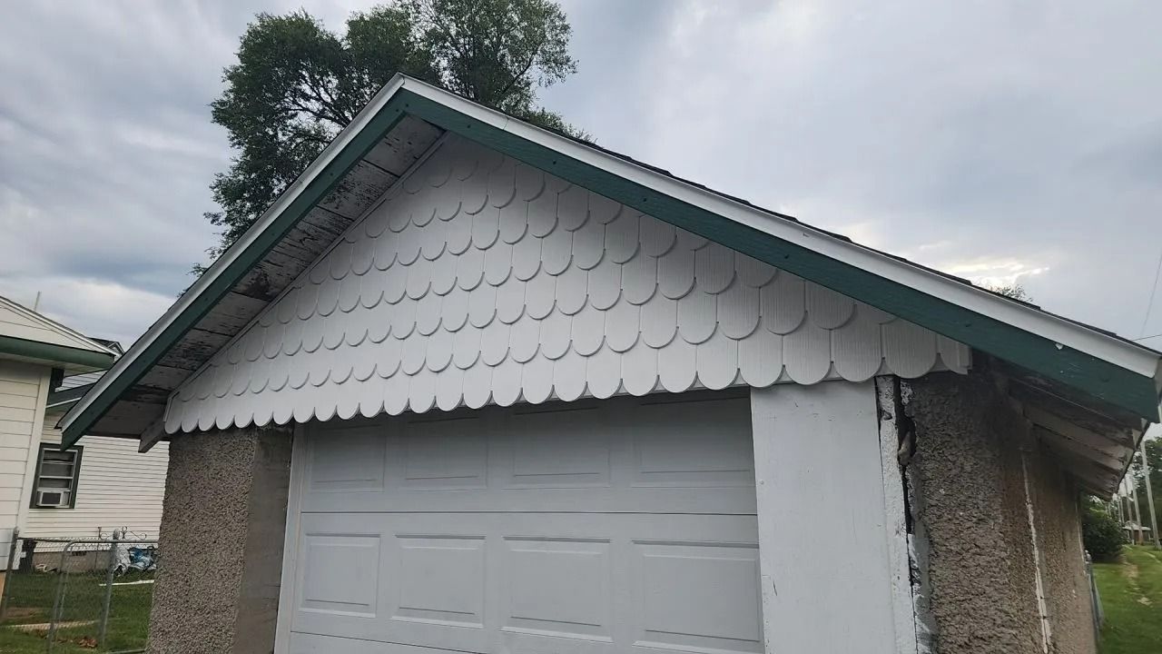 Garage with scallop-edged white siding and green trim under a cloudy sky.