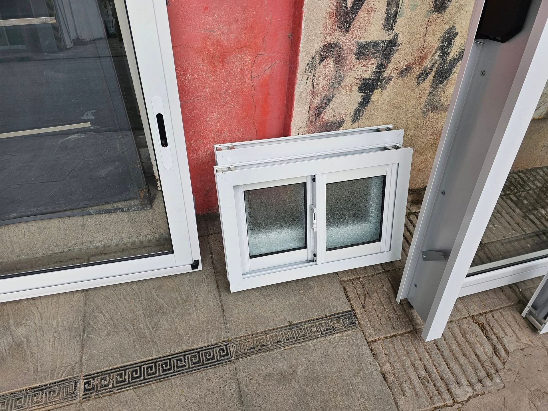 Las ventanas con marcos blancos se encuentran sobre una superficie de azulejos frente a una pared de color rojo y blanquecino.