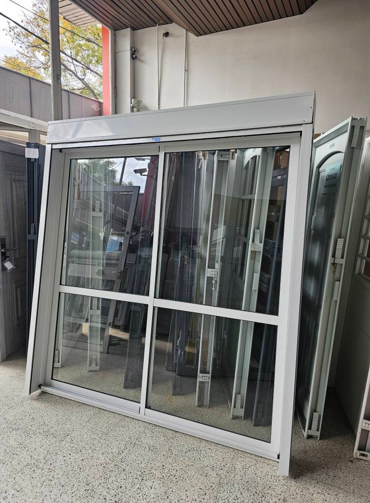 Puerta corrediza de vidrio con marco blanco, exhibida al aire libre con otras puertas.