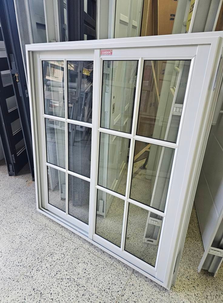 Ventana corrediza blanca con múltiples paneles de vidrio en un entorno de sala de exposición.