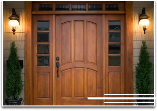 Puerta de entrada de madera con luces laterales, apliques de pared y vegetación.