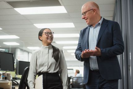 Gavin Mitchell, partner, and Jade Giang, manager, are walking down a hallway and talking together in an office environment.