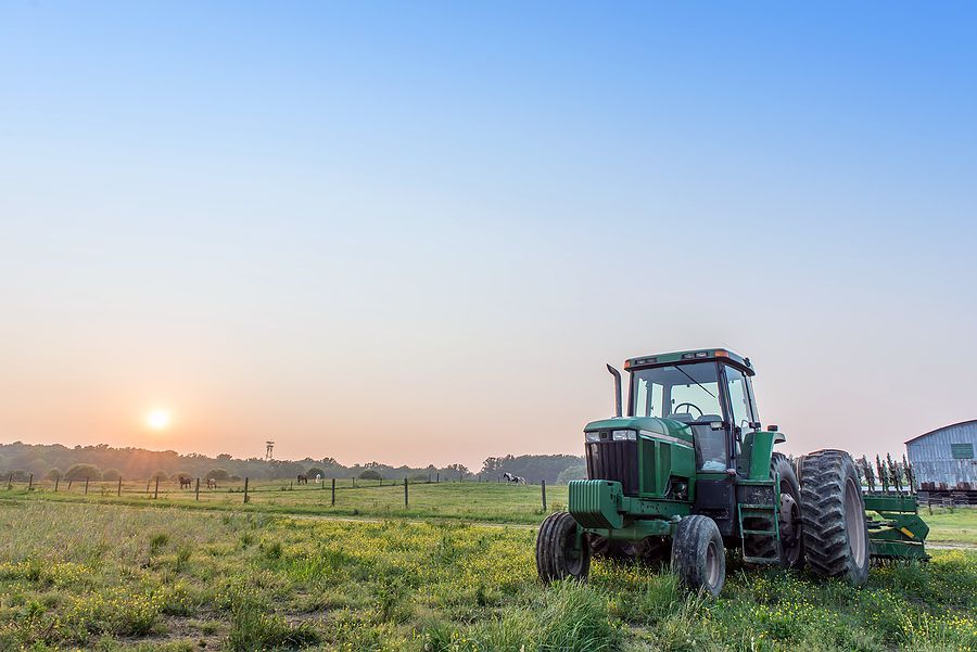 Agricultural landscape of a tractor in a field on a farm with the sun setting.