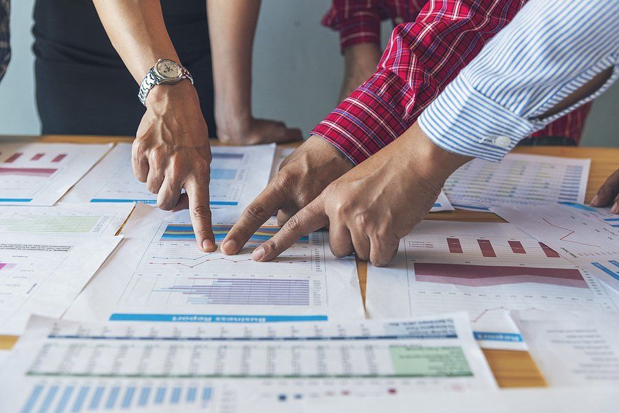 Business valuation meeting of people reviewing charts and numbers and pointing to a document.