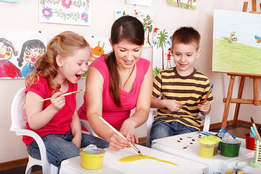 Children with teacher draw paints in play room. Child care.