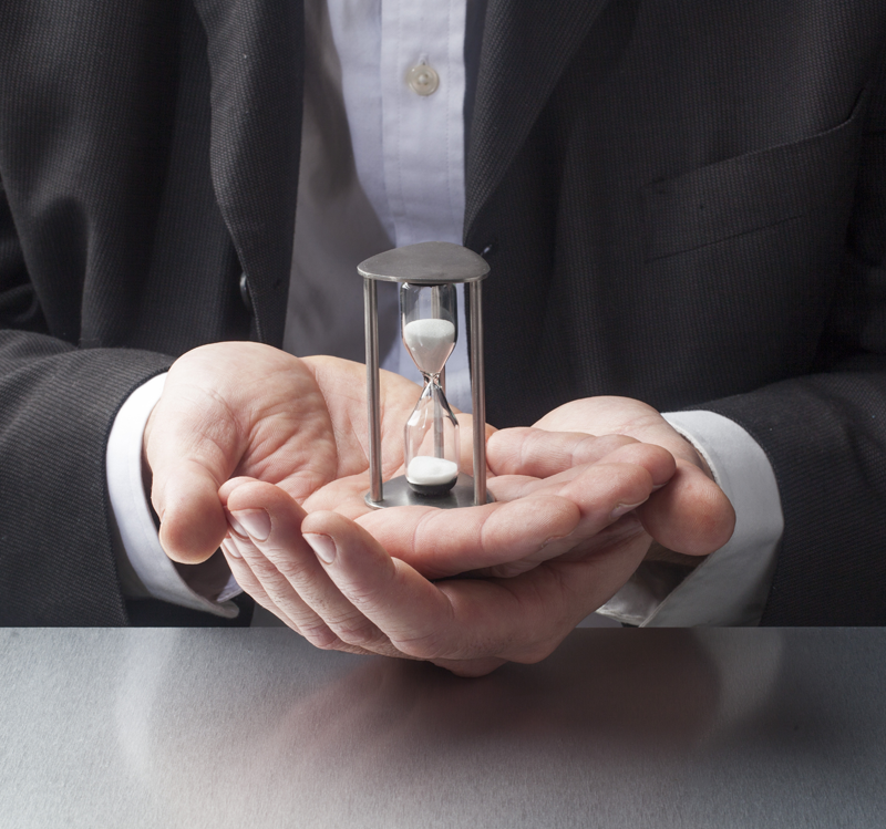 Business man at a desk with both hands out palms up holding a sand timer