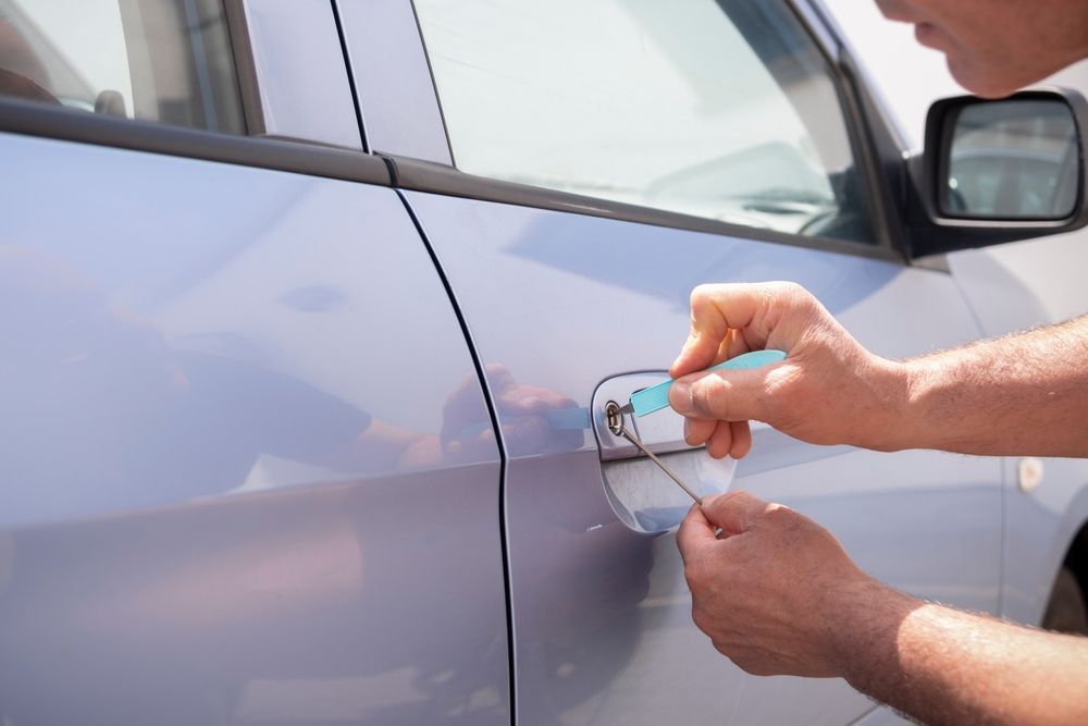 Person using lock picks to open a car door on a sunny day.