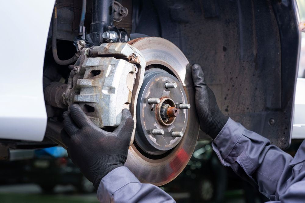 Mechanic's gloved hands near car brake disc and caliper, next to the wheel well.