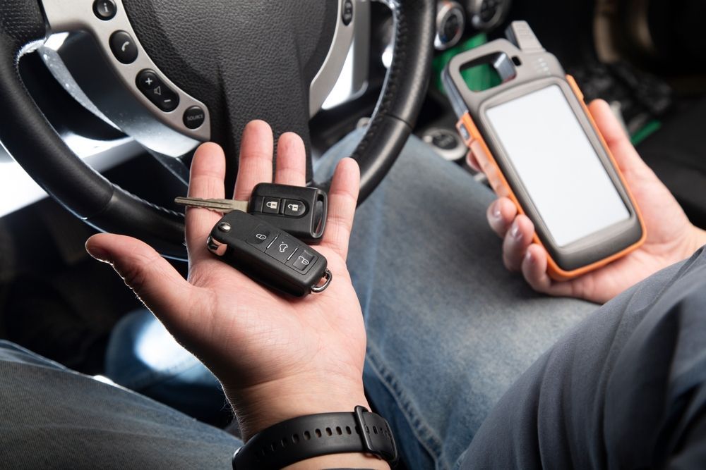 Person holding car keys and a diagnostic scanner inside a vehicle.
