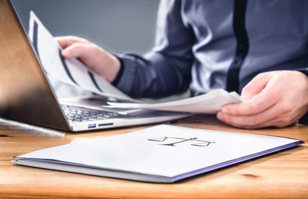Person Reviews Papers Near a Laptop, a Law Book — Hannaway Lawyers in Taree, NSW