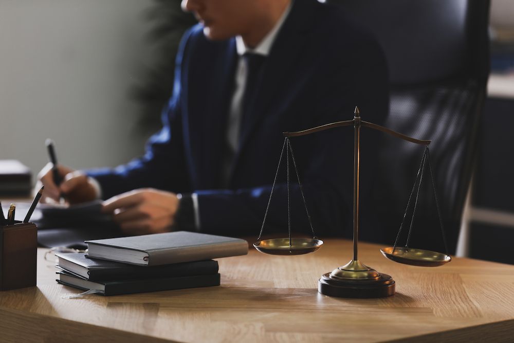 Scales of Justice on a Desk in Front of a Person in a Suit, Writing — Hannaway Lawyers in Port Macquarie, NSW