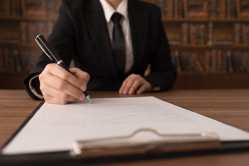 Person in Suit Signing a Document on a Clipboard With a Pen — Hannaway Lawyers in Forster, NSW